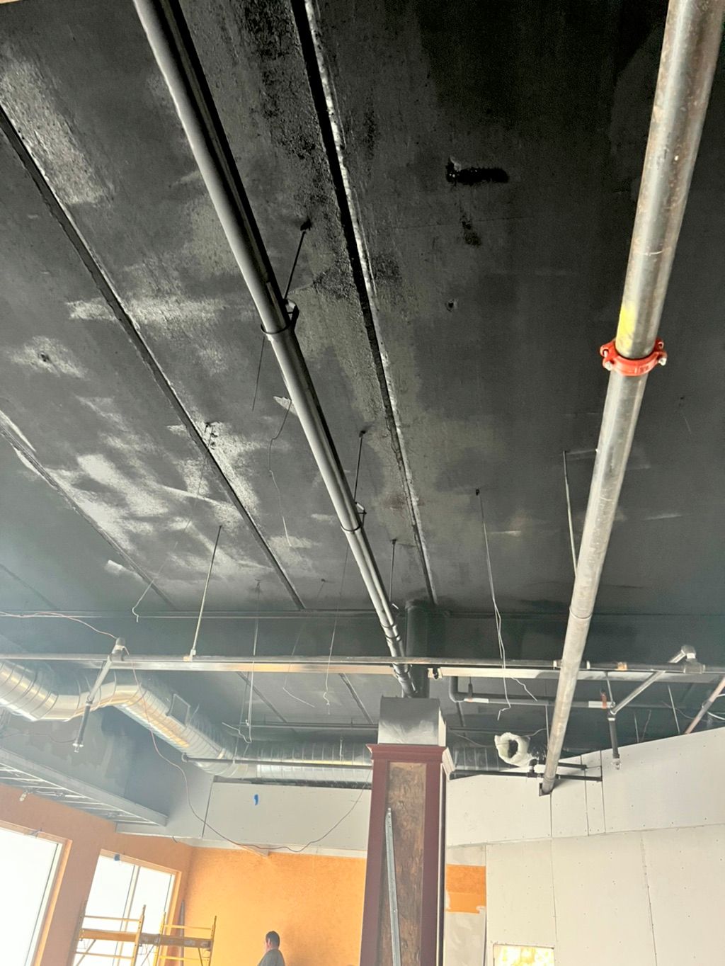 Real commercial interior project showing a dark open ceiling coating in progress
